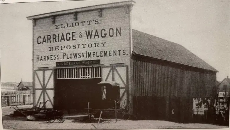 Old black-and-white photo of Elliott’s Carriage & Wagon Repository in Monument, Colorado, with a buggy parked in the open doorway