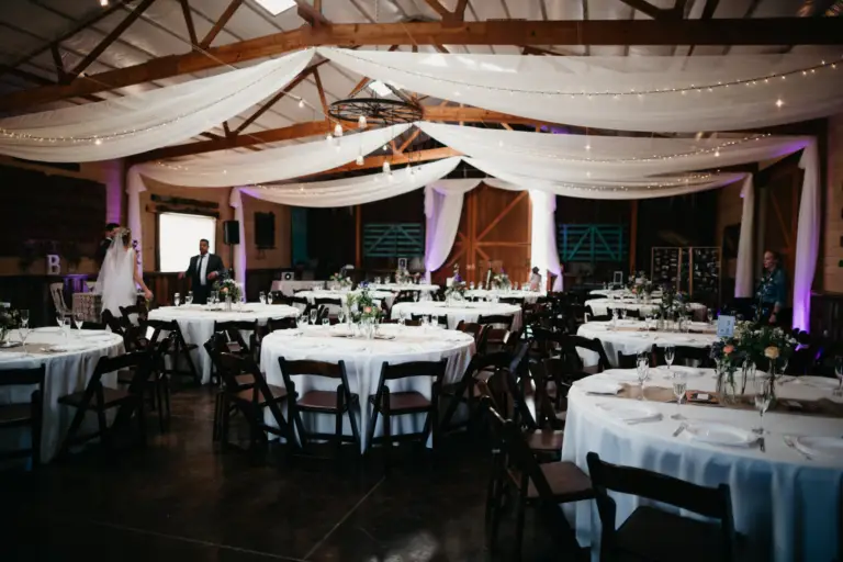 The Reception Barn at Younger Ranch set for a wedding, with draped fabric and string lights across the ceiling